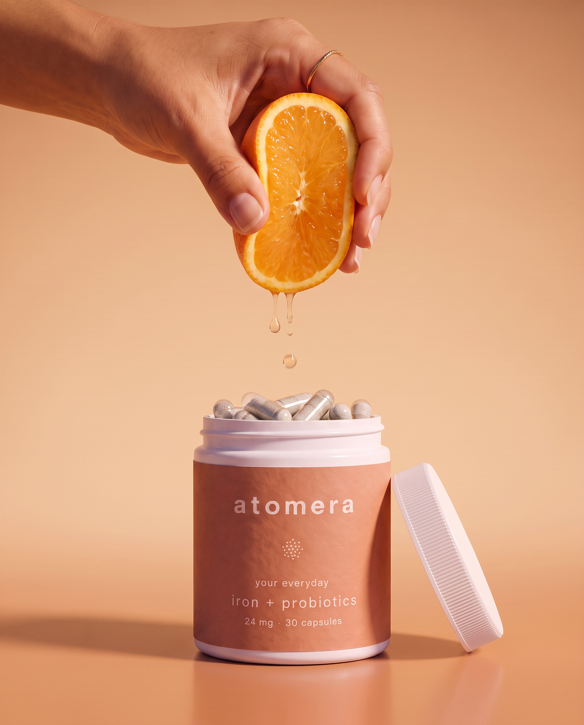 Hand squeezing half an orange over an open jar of atomera daily capsules