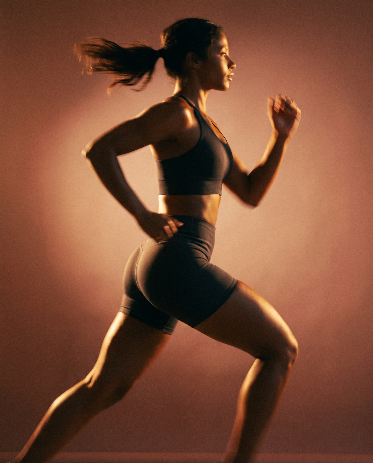 Woman in activewear running in profile against a warm, backlit terracotta background